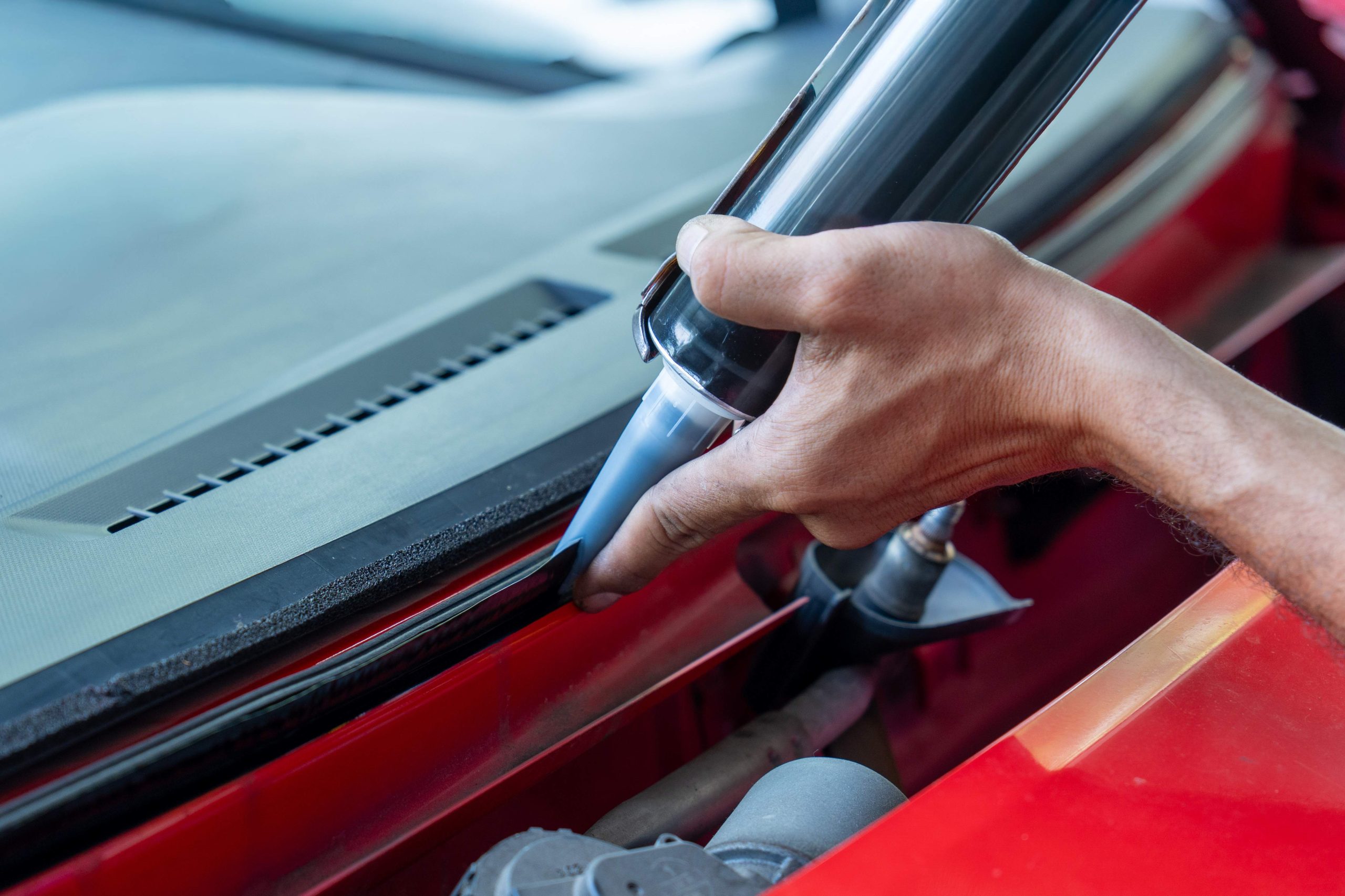 A hand is using a glass sealant to apply adhesive along the edge of a car's windshield. Fixing or replacing automotive parts concept.