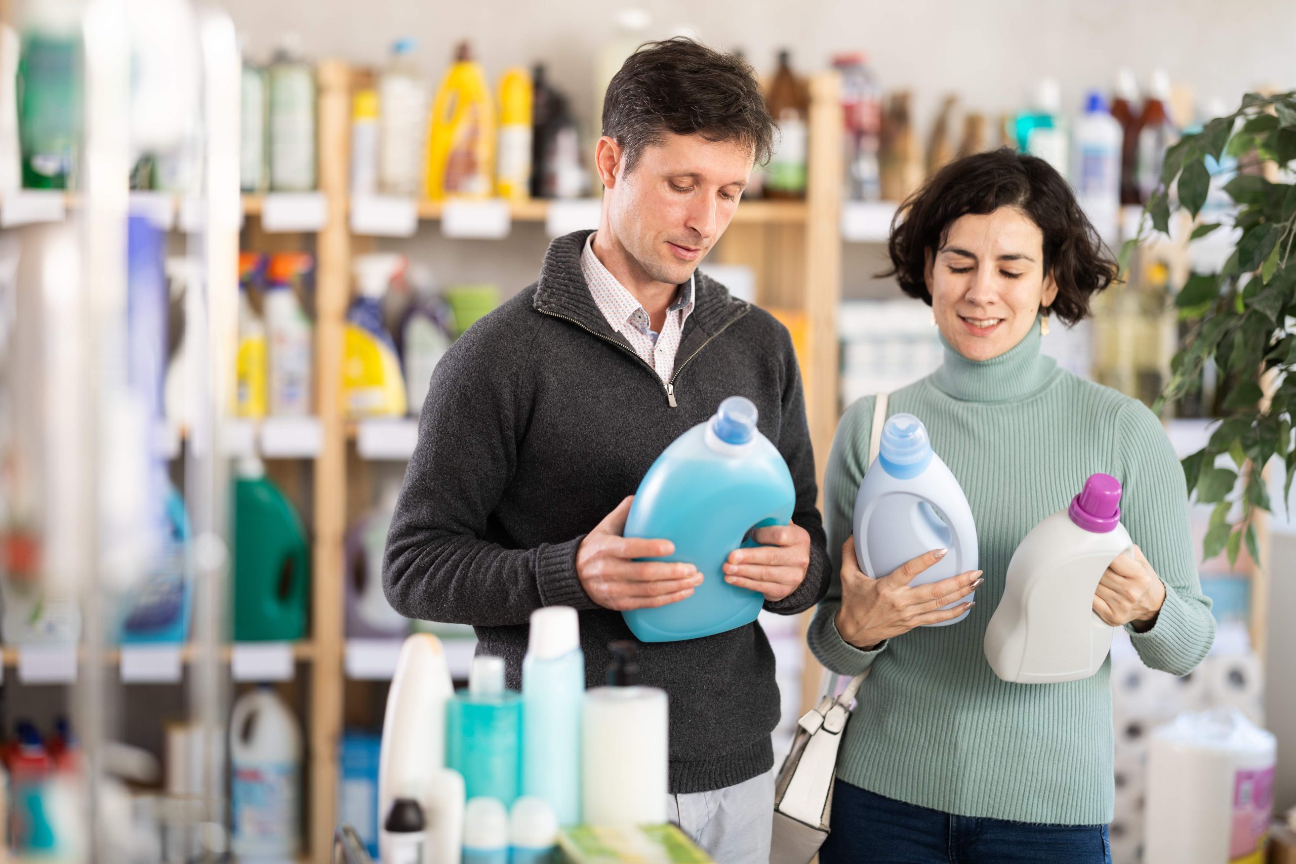 Married couple choosing home cleaner together while standing near the counter with household chemicals in the supermarket