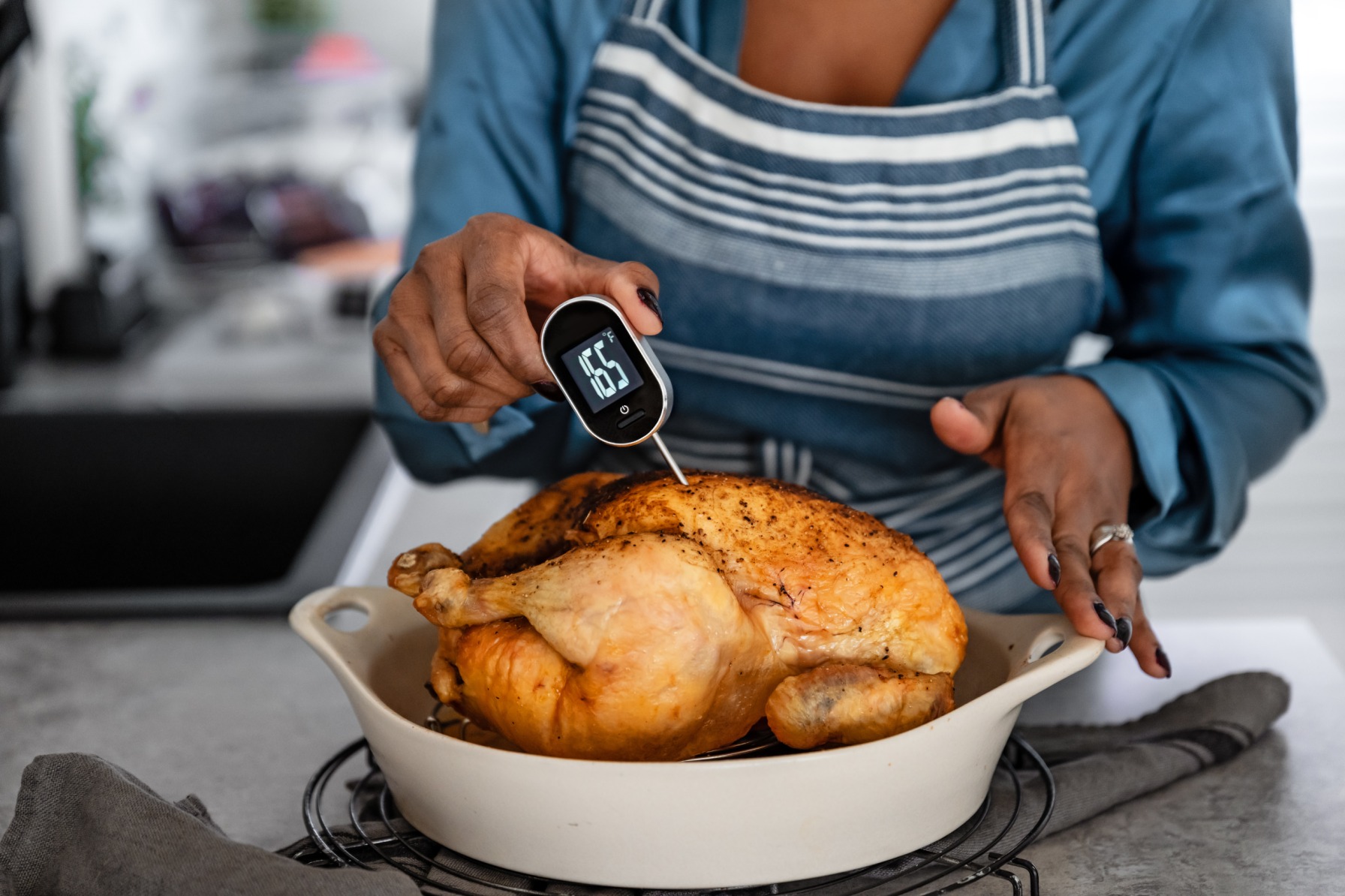 Woman sticking a meat thermoter into a piece of dead chicken