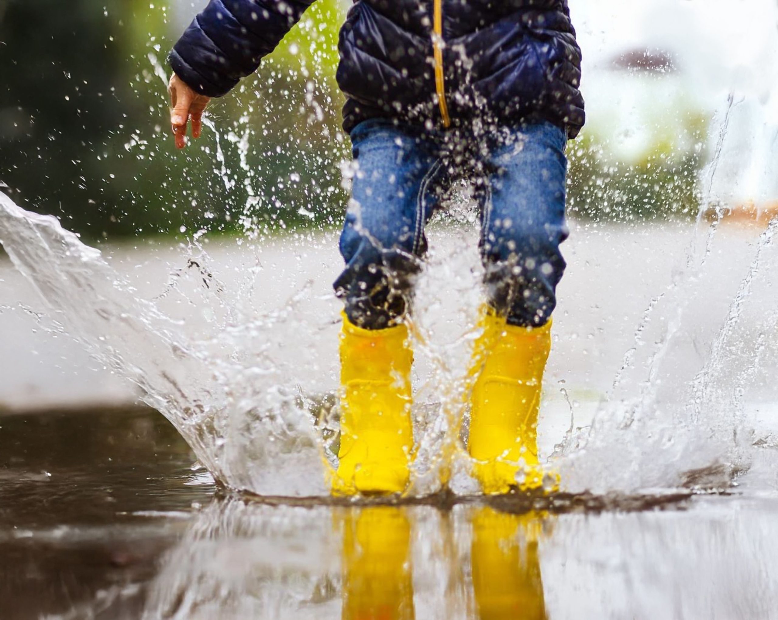 Child playing in the rain wearing rubber boots.