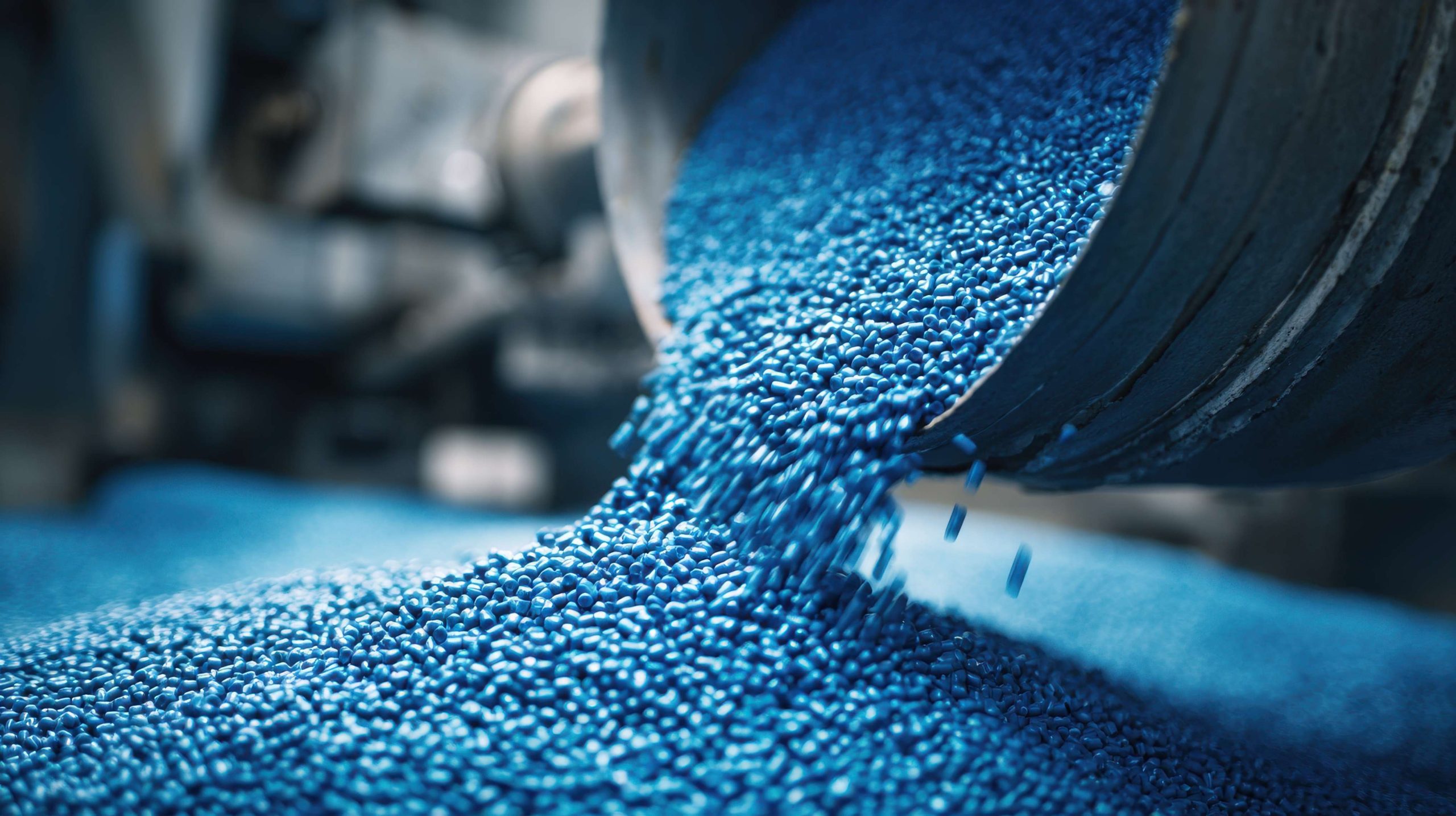 Close-up of blue plastic pellets pouring from an industrial hopper, raw materials for manufacturing process