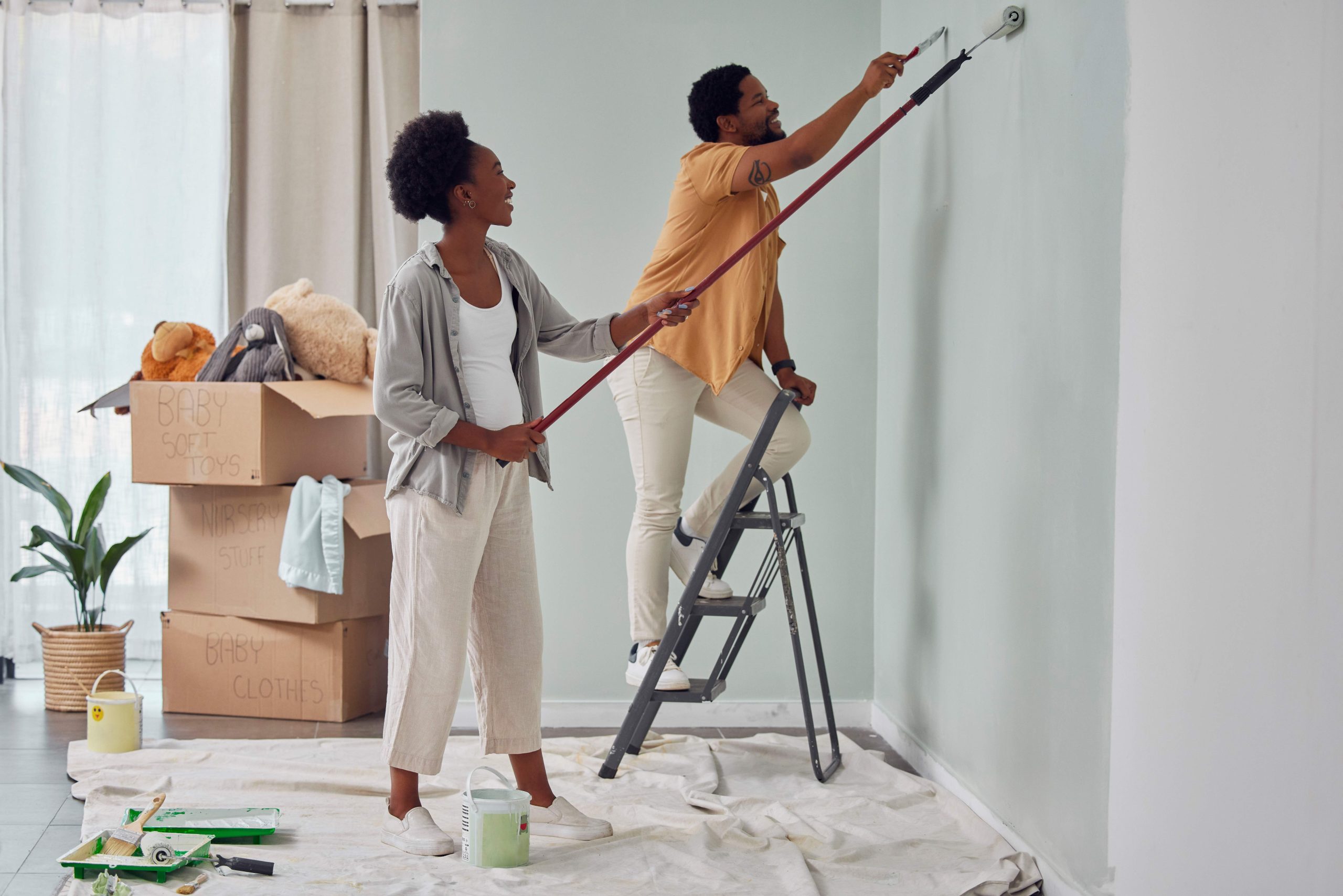 Painting, teamwork or black couple home renovation, diy or house remodel together with paintbrush or roller. Happy smile, woman and African man love working on wall with partnership or collaboration.