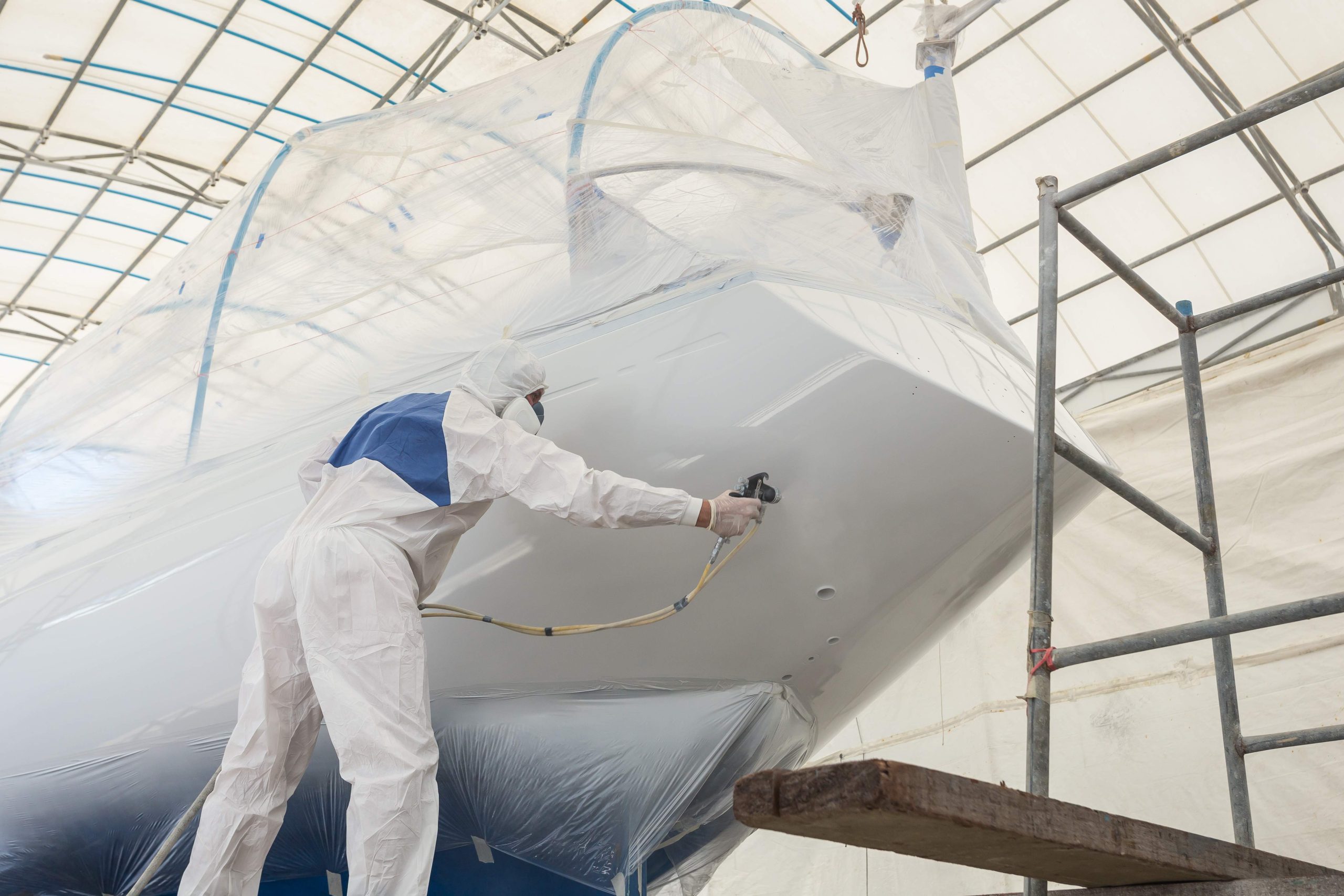 Worker wearing protective uniform and spraying paint to the boat, Maintenance concept