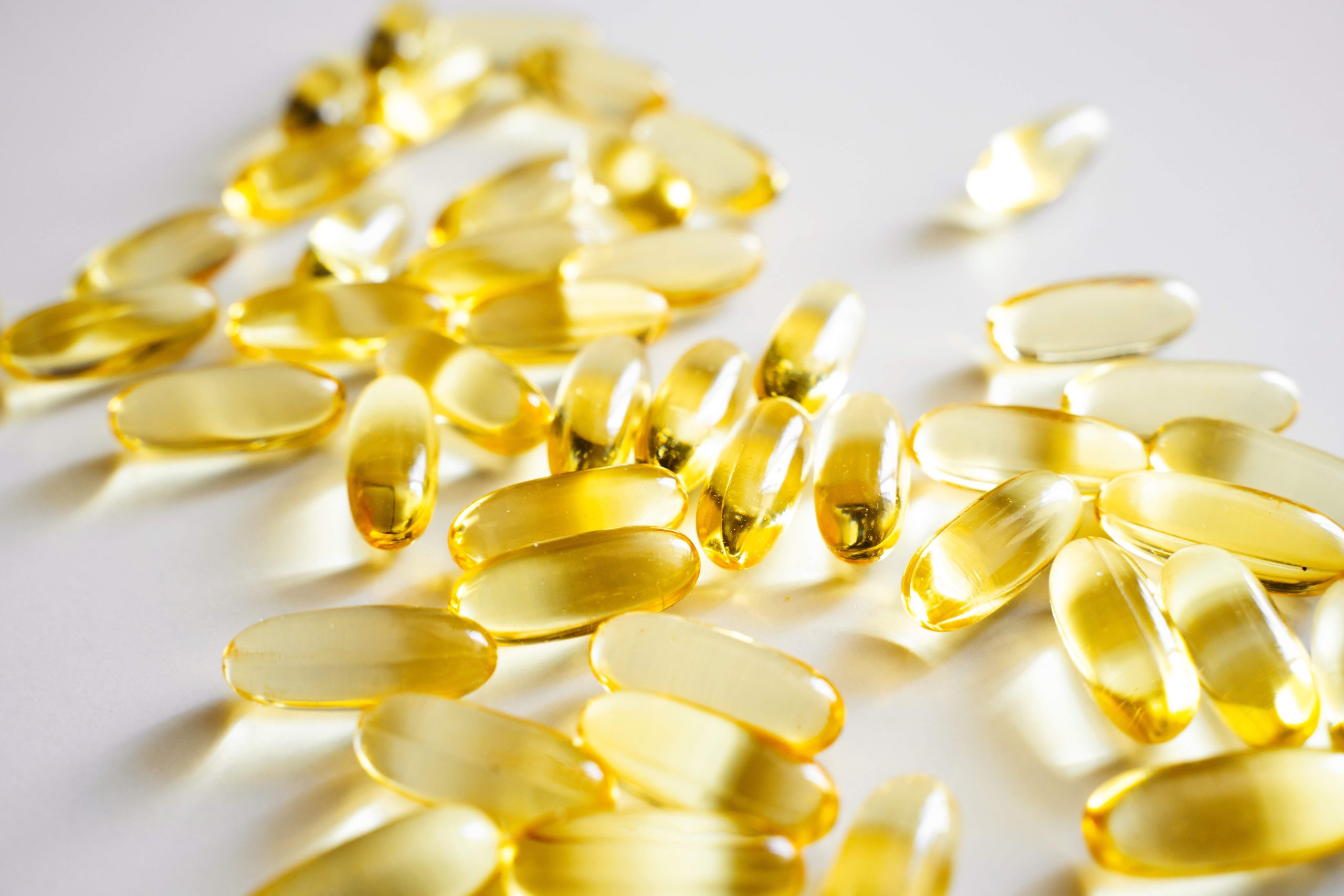 Close up view of yellow omega fish oil capsules on white background, symbolizing health, vitamins, nutritional supplements and natural wellness care.