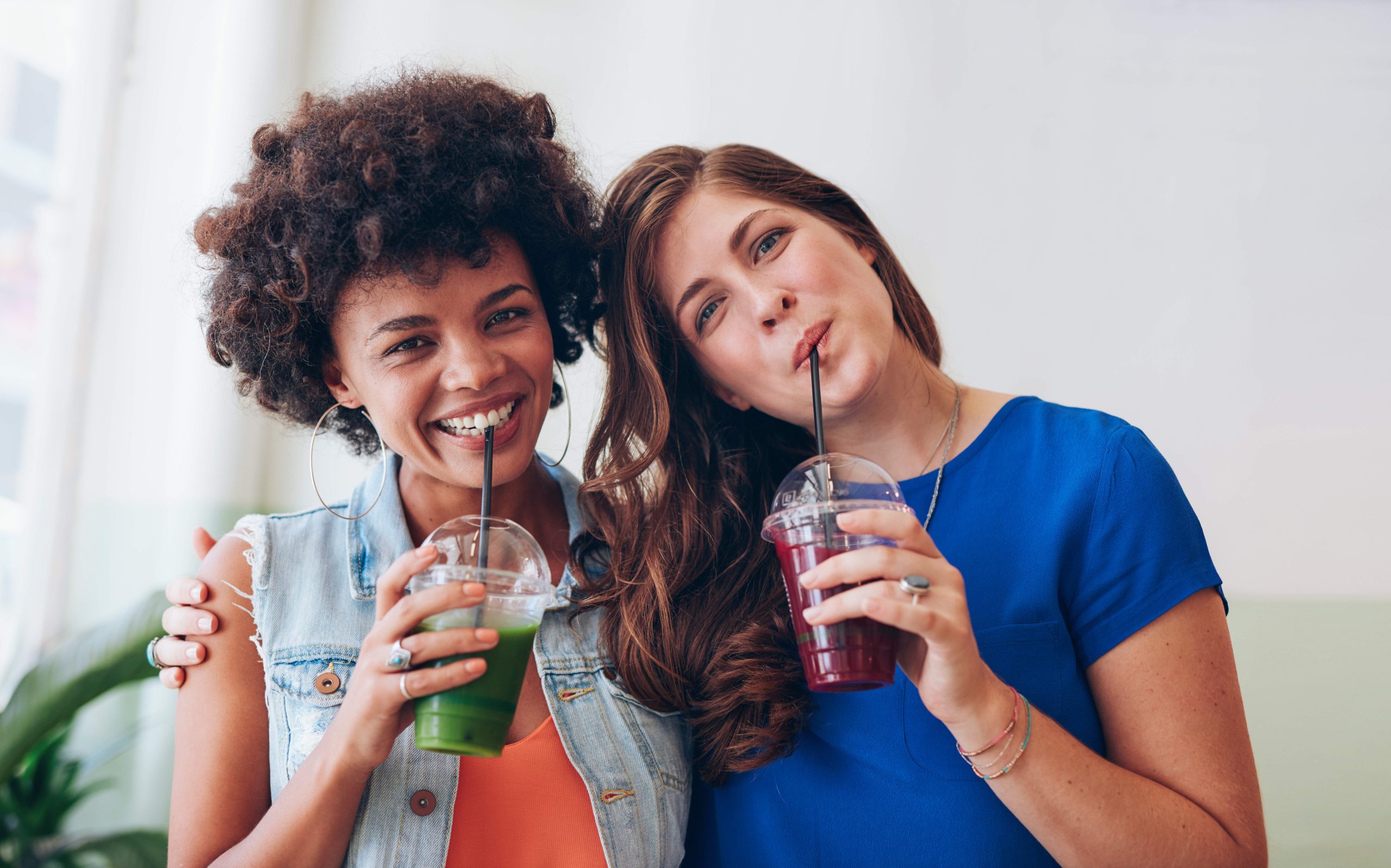 Portrait of beautiful young women drinking fresh juice together. Female friends standing together having smoothies.