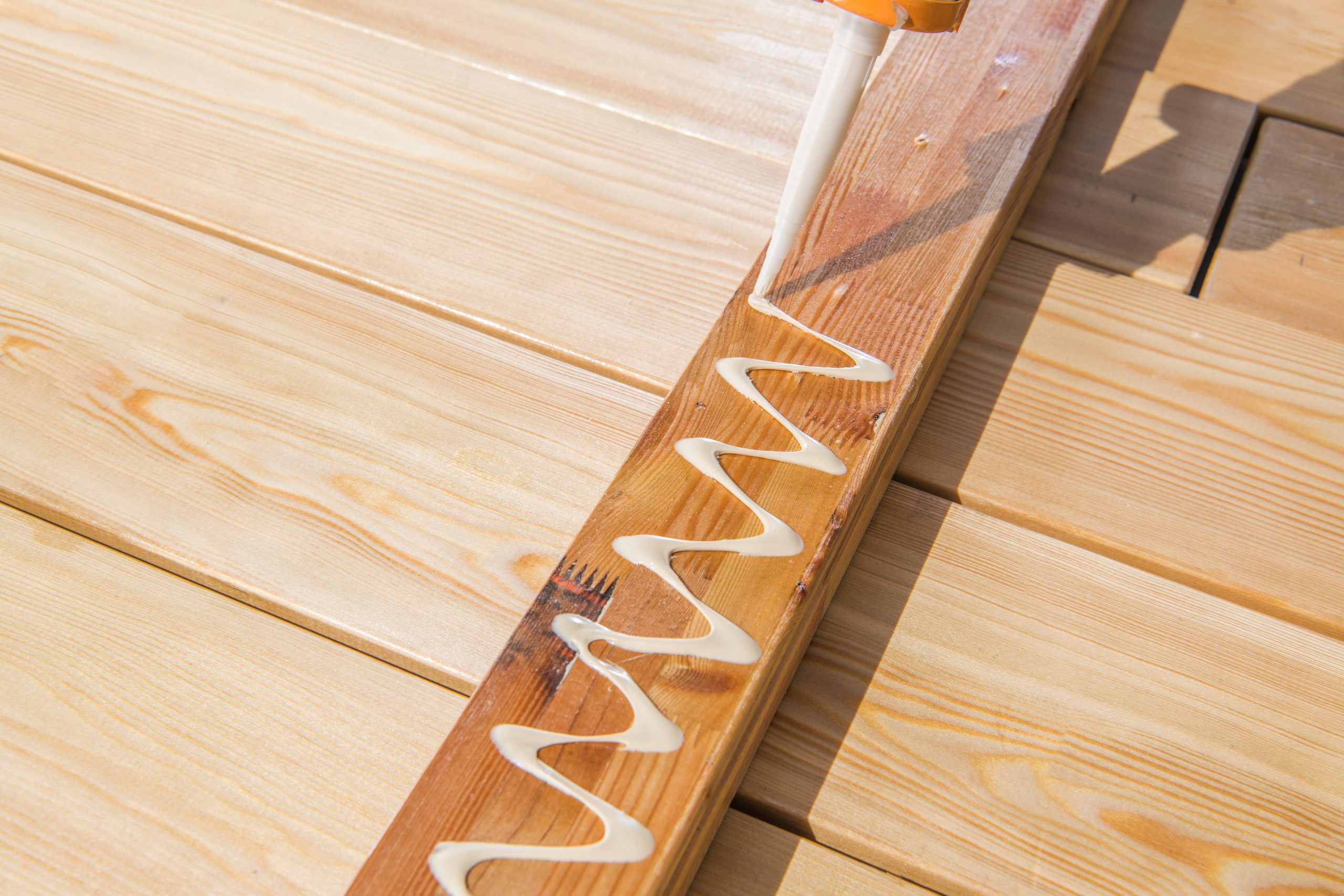 Wood glue is being applied to a wooden plank in a zigzag pattern, showcasing an essential step in joining pieces for a construction or crafting task.