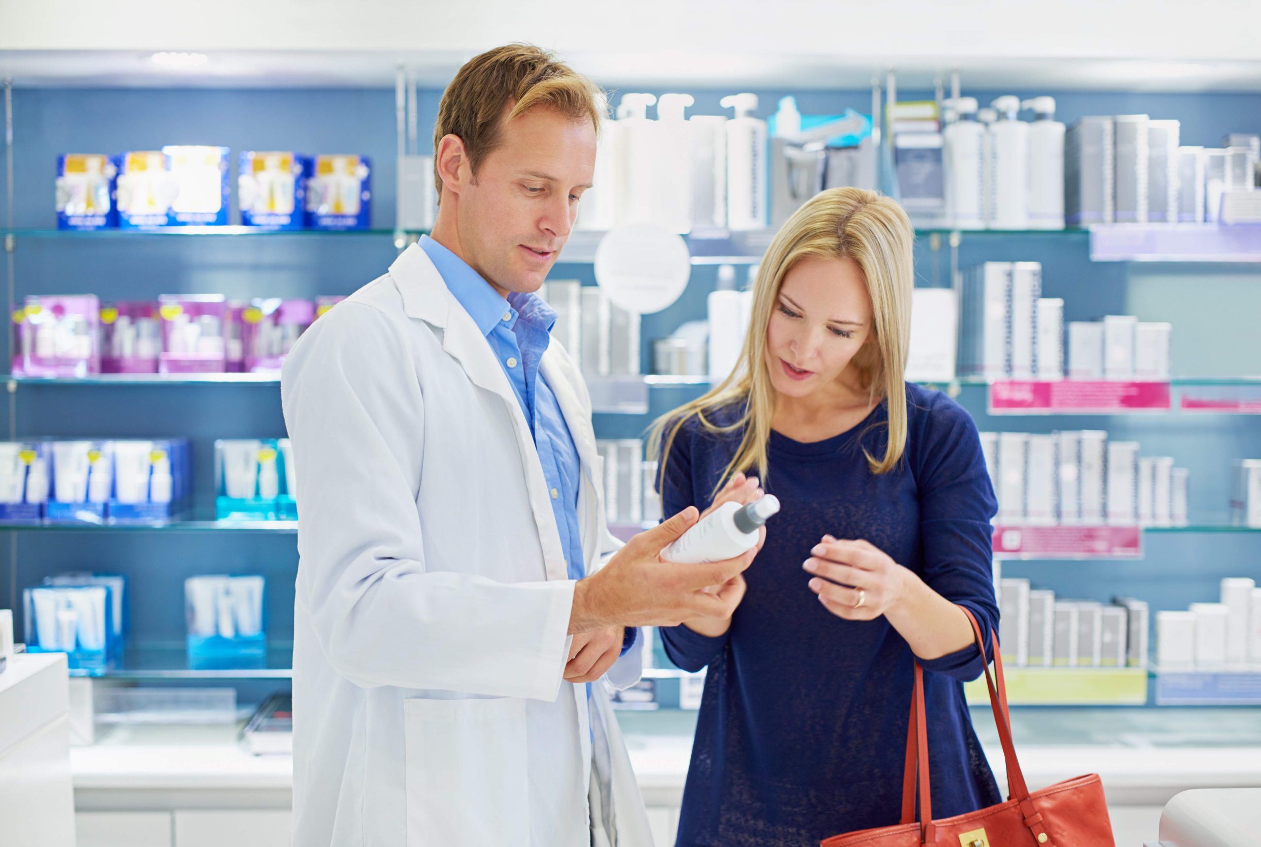 Pharmacy, man and woman with cosmetics, advice and reading instructions on skincare bottle together in shop. Dermatology, pharmacist and customer with help checking label on beauty product in store.