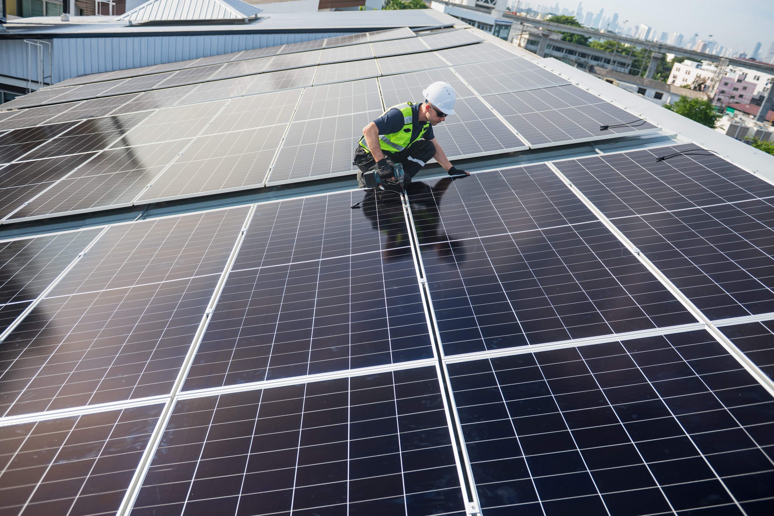 Technician installing solar panels on factory roof for green energy. A skilled technician in safety gear is working on a solar panel installation on rooftop. clean energy renewable power technology.