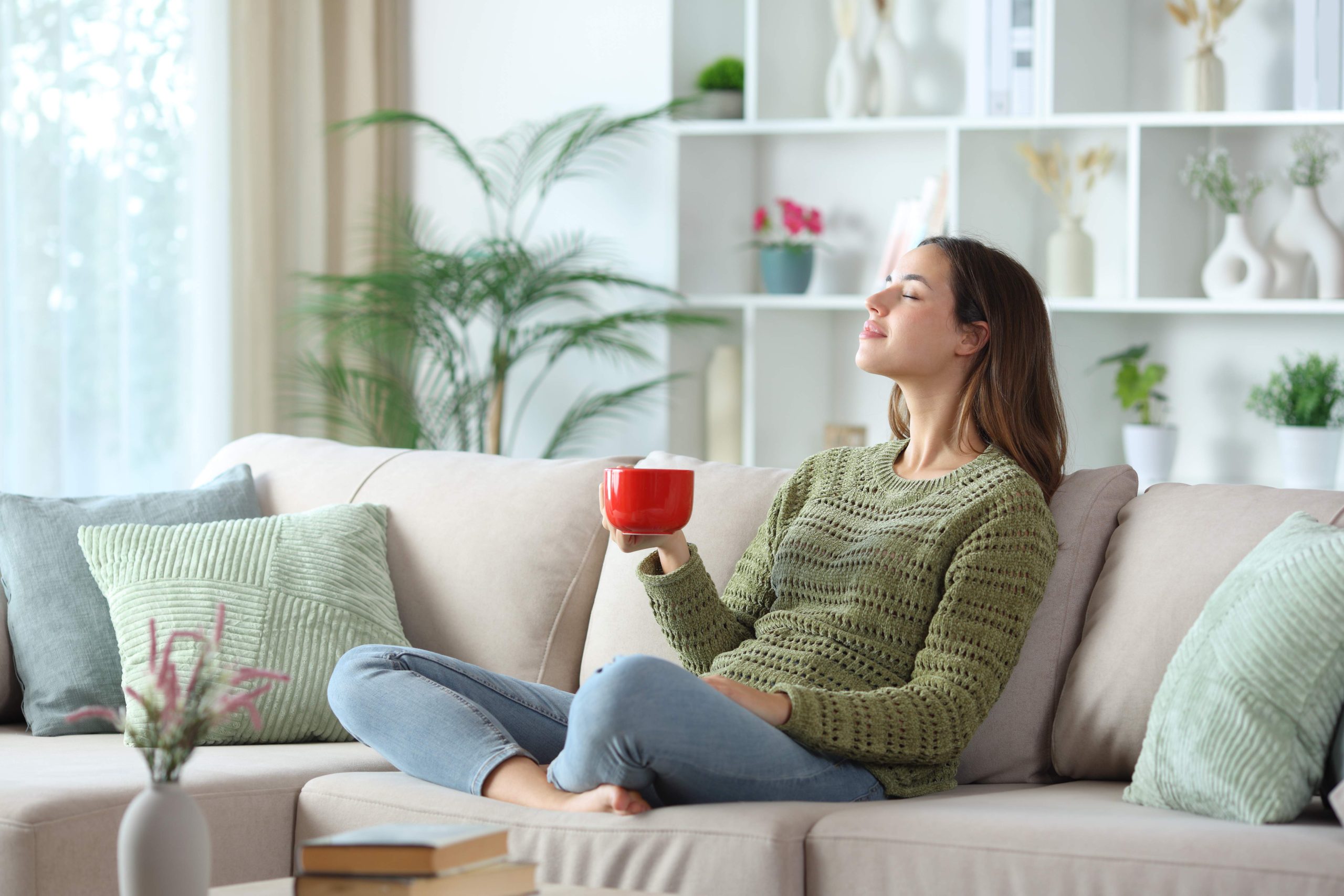 Relaxed woman in green breathing and drinking coffee sitting on a sofa at home