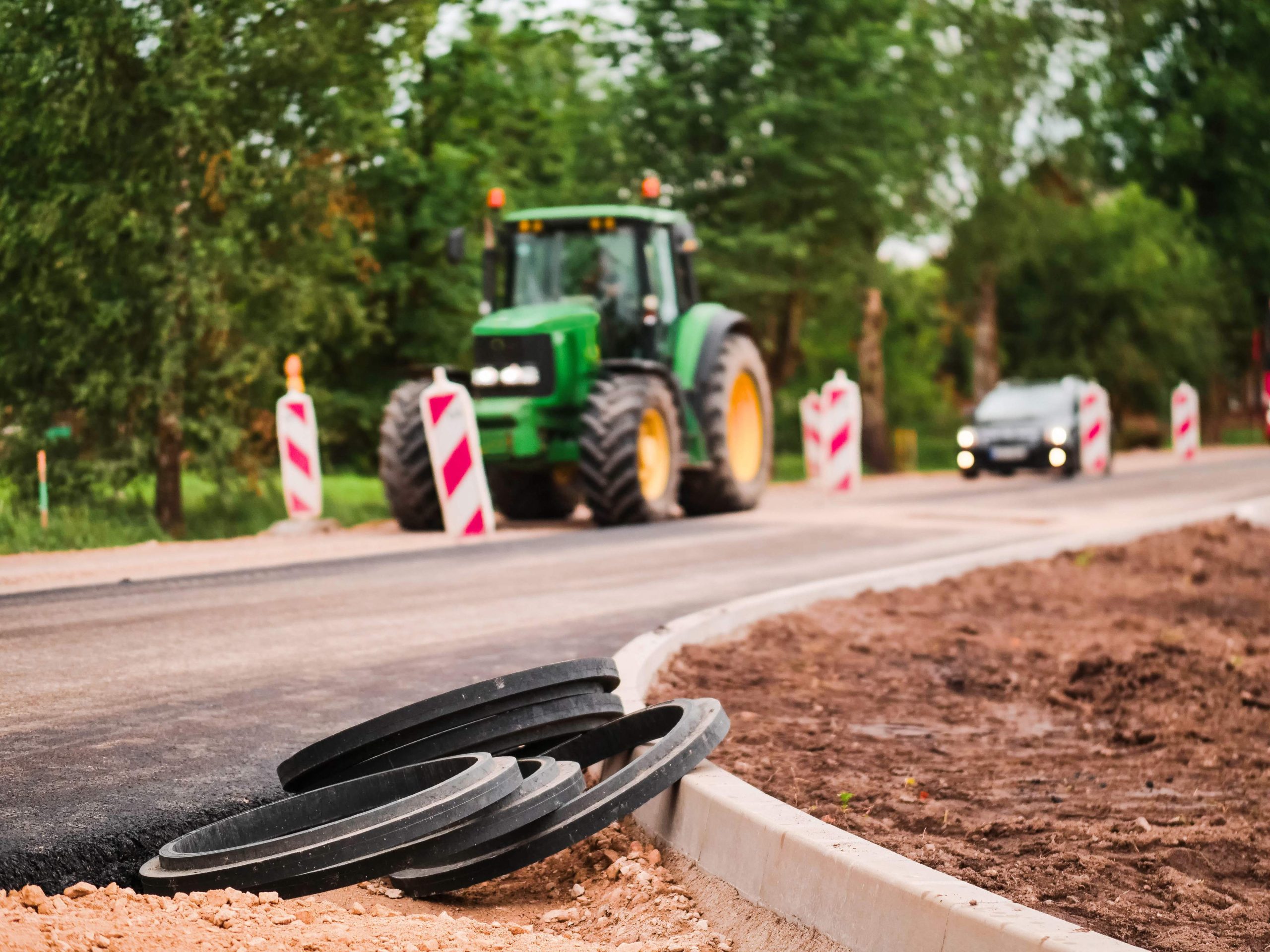 Road works in a rural country side area. Plastic fittings and freshly laid asphalt in foreground, safety security signs and tractor out of focus in the background.