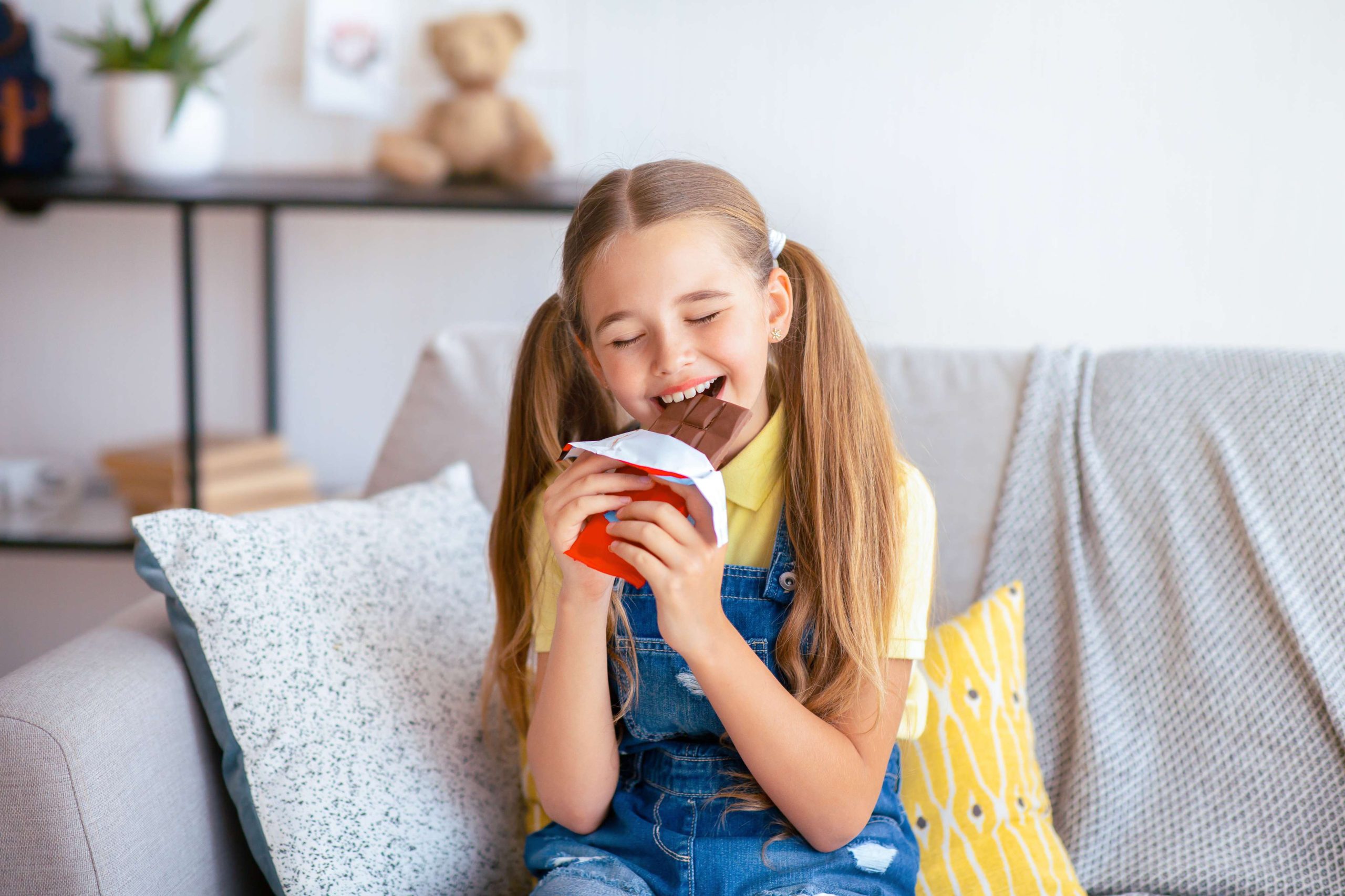 Happy girl eating chocolate sitting on a couch in the living room at home.
