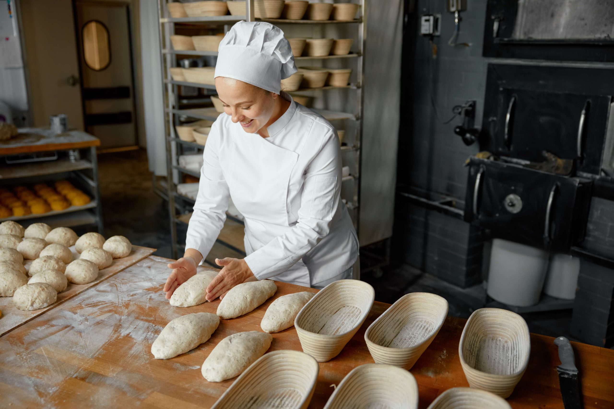 Professional positive woman baker forming loaf from raw dough.