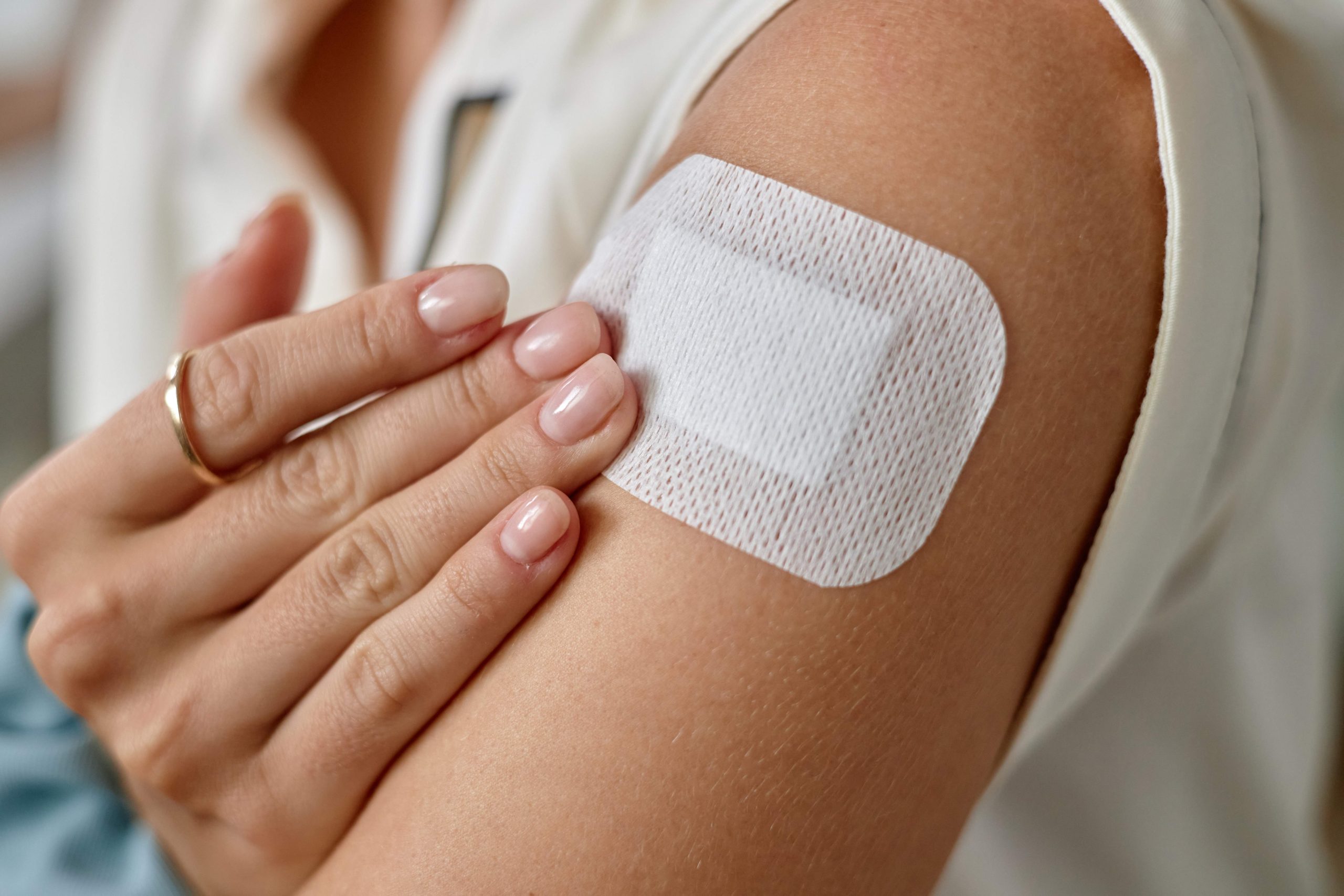 Woman touching adhesive bandage on upper arm, showing manicured hand with natural nails, birth control concept