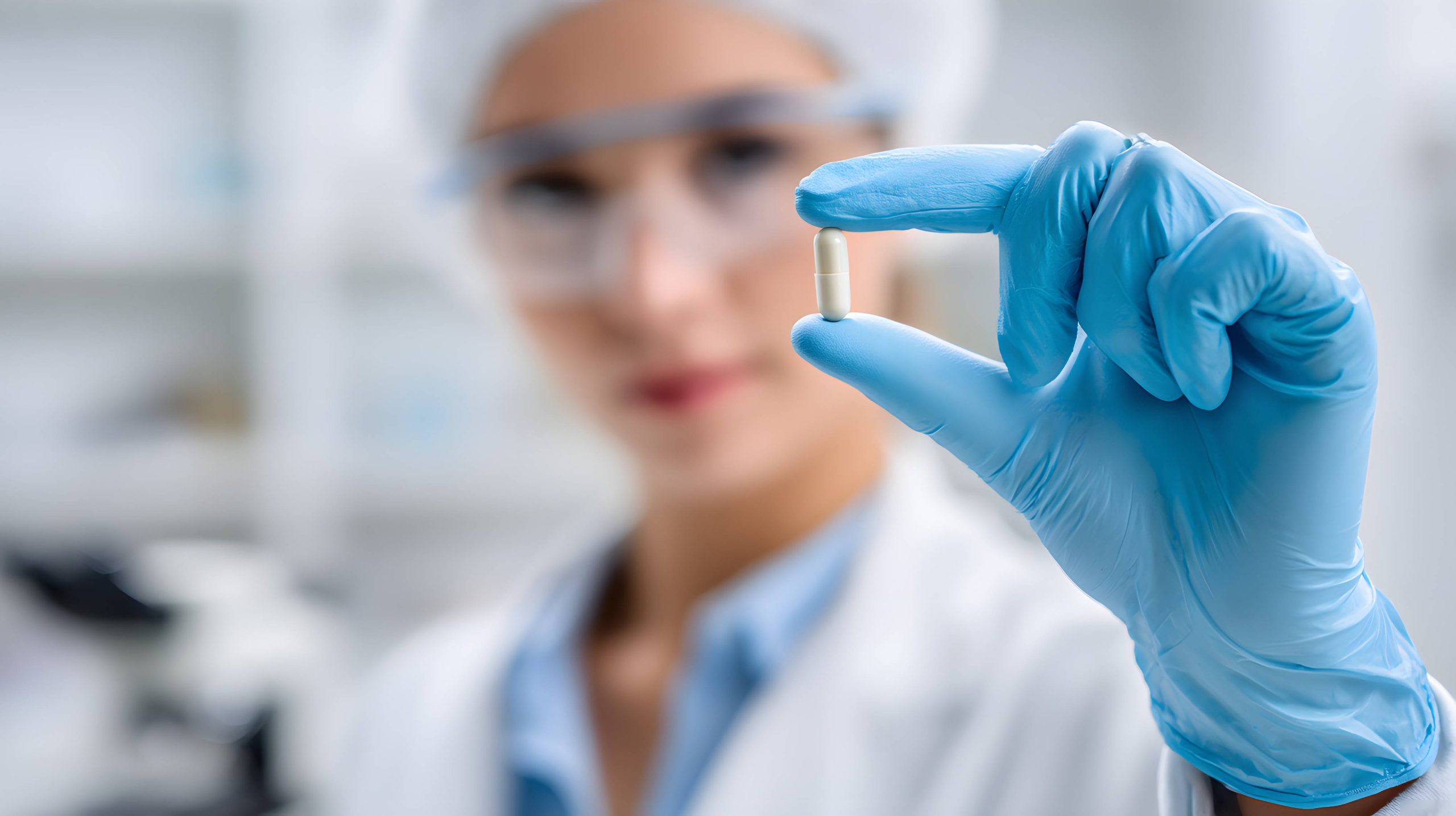 A female doctor holds a small capsule against a research lab background.